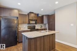Functional kitchen featuring an island with an integrated sink, dark wood-finish cabinetry, granite-style countertops, black appliances, and recessed lighting - 