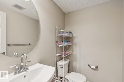 Bathroom featuring a white pedestal sink with chrome faucet, circular wall mirror, a white toilet, and light neutral wall paint - 