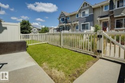 Private fenced yard featuring a concrete patio, a section of lawn, and a white picket fence with gate access - 