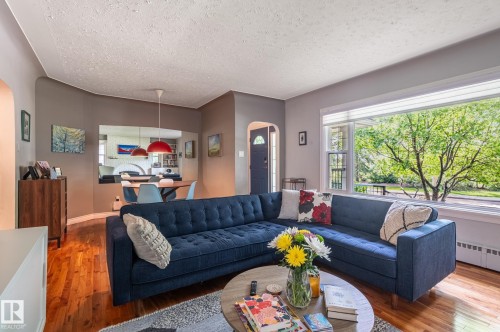 Living room featuring hardwood flooring, a large picture window, and an arched doorway - 11634 74 Avenue Nw, Edmonton, AB 