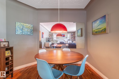 Dining area featuring wood-finish flooring, a contemporary red pendant light fixture, and a large wall mirror - 11634 74 Avenue Nw, Edmonton, AB 