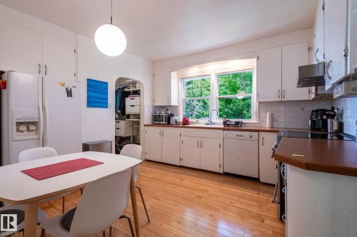 Kitchen featuring wood-finish flooring, white cabinetry, a built-in dishwasher, and a window above the sink - 11634 74 Avenue Nw, Edmonton, AB 