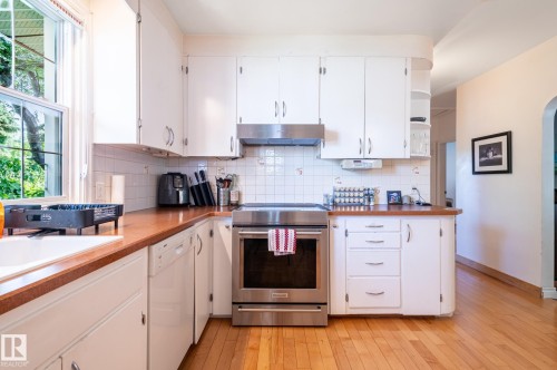 Bright kitchen featuring white cabinetry, light wood-finish flooring, and a stainless steel range with overhead ventilation - 11634 74 Avenue Nw, Edmonton, AB 