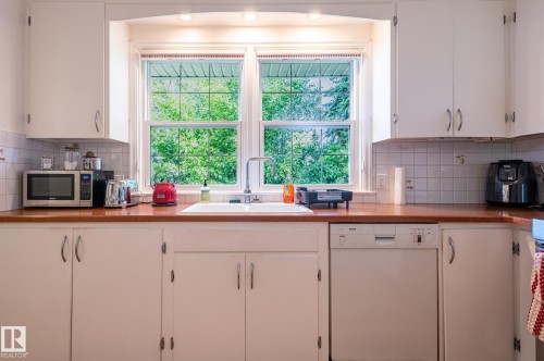 Kitchen featuring a double window above the sink, white cabinetry, light-toned tiled backsplash, and a built-in dishwasher - 11634 74 Avenue Nw, Edmonton, AB 