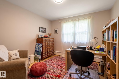 Neutral-toned room featuring light wood-finish flooring, a large window with sheer white curtains, and a built-in light wood shelving unit - 11634 74 Avenue Nw, Edmonton, AB 