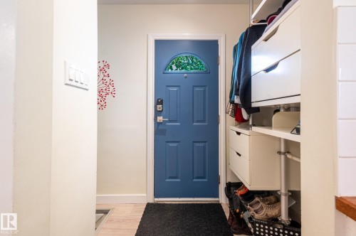 Entryway featuring a paneled blue door with an arched window, wood-finish flooring, and a built-in storage system with shelving and drawers - 11634 74 Avenue Nw, Edmonton, AB 