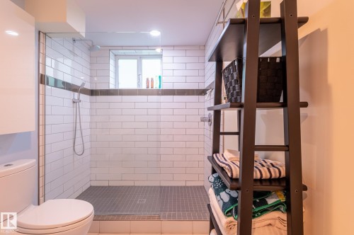 Bathroom featuring a glass-enclosed shower with white subway tile, a dark accent tile band, and a window - 11634 74 Avenue Nw, Edmonton, AB 
