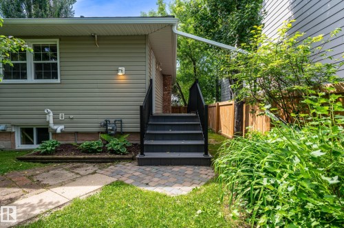 Exterior featuring light-colored siding, a prominent staircase with dark railings, and a paver stone landing - 11634 74 Avenue Nw, Edmonton, AB 