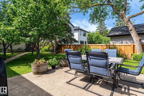 Concrete patio with a dining set, surrounded by a manicured lawn and mature trees - 11634 74 Avenue Nw, Edmonton, AB 