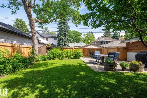Spacious backyard featuring a manicured lawn, concrete patio area, perimeter fencing, mature trees, and established shrubbery - 11634 74 Avenue Nw, Edmonton, AB 