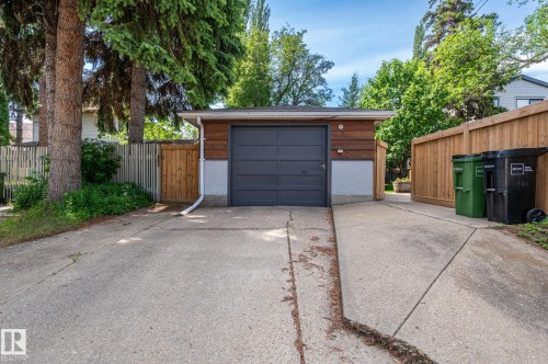 Detached garage featuring a dark gray sectional door, wood-paneled siding, and a concrete driveway - 11634 74 Avenue Nw, Edmonton, AB 