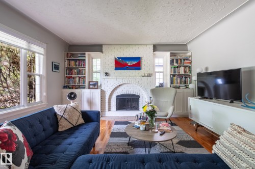 Living area featuring a painted brick fireplace with an arched opening, flanked by built-in bookcases and cabinetry - 11634 74 Avenue Nw, Edmonton, AB 