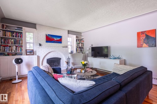 Living room featuring a white brick fireplace with an arched firebox opening, flanked by built-in shelving and cabinetry - 11634 74 Avenue Nw, Edmonton, AB 