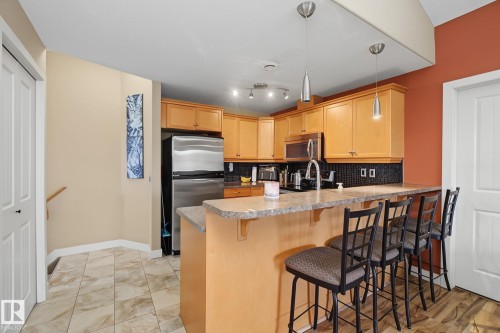 Kitchen featuring light wood cabinetry, stainless steel refrigerator and microwave, dark tile backsplash, and a breakfast bar with pendant lighting - 30 2565 Hanna Crescent, Edmonton, AB 