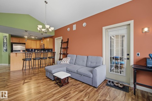Open-concept living area featuring wood-finish flooring, a kitchen with a breakfast bar, stainless steel appliances, a vaulted ceiling, and a French door with an integrated blind - 30 2565 Hanna Crescent, Edmonton, AB 