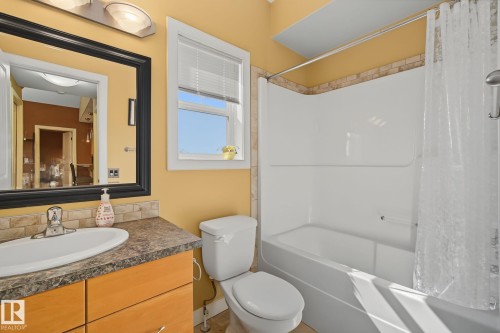 Bathroom featuring a white bathtub and shower combination with a tile surround, a single vanity with a dark countertop, an oval undermount sink, and a framed mirror with overhead lighting - 30 2565 Hanna Crescent, Edmonton, AB 