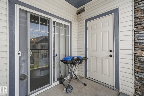 Exterior patio area featuring horizontal siding, stacked stone accents, a paneled entry door with matte black hardware, and a sliding glass door with a screen - 30 2565 Hanna Crescent, Edmonton, AB 