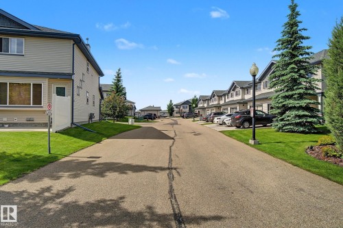 Residential street featuring a row of multi-story properties with siding exteriors, dark shingled roofs, and attached garages - 30 2565 Hanna Crescent, Edmonton, AB 