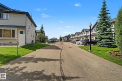 Residential street featuring a row of multi-story properties with siding exteriors, dark shingled roofs, and attached garages - 