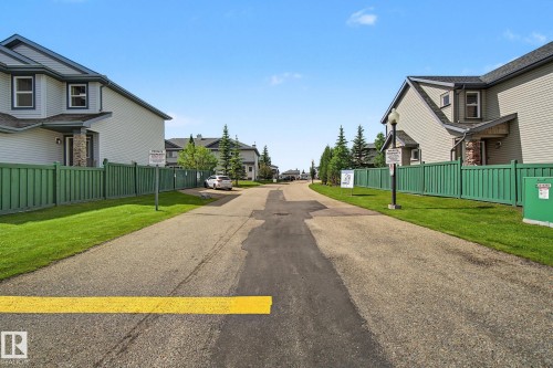 Residential street with asphalt paving and a yellow traffic marking, flanked by green privacy fencing - 30 2565 Hanna Crescent, Edmonton, AB 