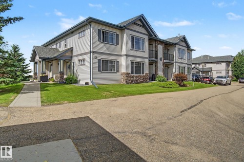 Multi-story residential building featuring light-colored siding, stone accents, dark-framed windows with shutters, and gabled rooflines - 30 2565 Hanna Crescent, Edmonton, AB 