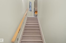 Carpeted staircase with light wood-finish handrail and integrated wall lighting - 