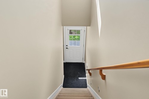 Carpeted staircase with a natural wood handrail, leading to an exterior door with multiple window panes, set against neutral wall tones - 30 2565 Hanna Crescent, Edmonton, AB 