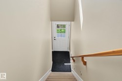 Carpeted staircase with a natural wood handrail, leading to an exterior door with multiple window panes, set against neutral wall tones - 