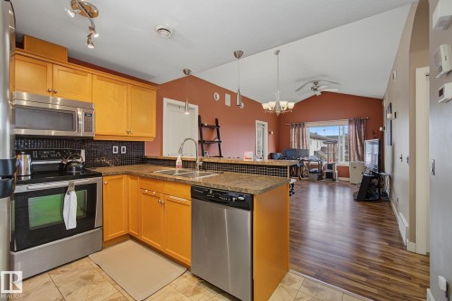 Open-concept kitchen featuring stainless steel appliances, light wood cabinetry, and a dark tile backsplash - 30 2565 Hanna Crescent, Edmonton, AB 