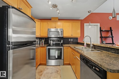 U-shaped kitchen featuring light wood cabinetry, stainless steel appliances, dark tile backsplash, and a double basin sink - 30 2565 Hanna Crescent, Edmonton, AB 