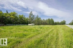 Expansive green space featuring natural grass, perimeter fencing, and mature trees - 