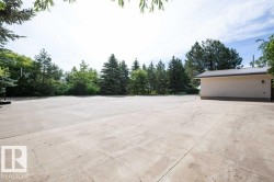 Expansive concrete slab with surrounding mature trees and a detached structure featuring stucco siding and a metal roof - 