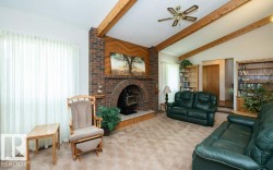 Expansive living area featuring a brick fireplace with a wood-burning stove insert, vaulted ceiling with exposed wood beams, and built-in wood bookcases - 