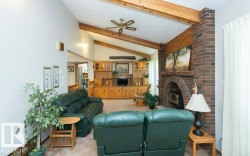 Vaulted ceiling with exposed wood beams, a prominent brick fireplace, and built-in wood cabinetry characterize this living space - 