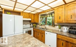 Kitchen featuring a coffered ceiling with diffused lighting, wood-finish cabinetry, a double basin sink, and a multi-toned backsplash - 
