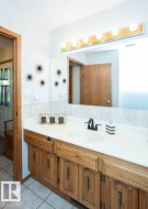 Bathroom vanity featuring a light wood-finish cabinet with brass hardware, a white solid-surface countertop with an integrated sink, and a black faucet - 