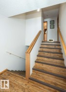 Multi-level staircase featuring wood-finish treads with dark risers, a wood handrail, and white walls - 