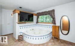 Corner soaking tub with tiled surround, wood-framed window, and integrated shelving - 