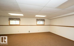 Finished room featuring light brown carpeting, white walls with a wood accent rail, and a drop ceiling with recessed lighting - 