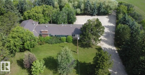 Expansive property featuring a brown shingled roof, multiple mature trees, a well-maintained lawn, and a gravel driveway - 26530 Twp Rd 590, Rural Westlock County, AB - Outdoor With View
