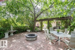 Expansive stamped concrete patio featuring a fire pit, decorative fountain, and a wooden pergola with mature climbing vines - 