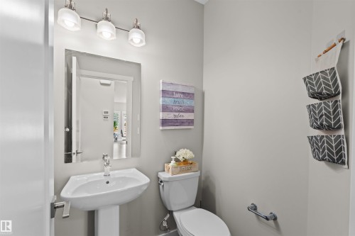 Powder room featuring a pedestal sink, wall-mounted mirror, and a three-light vanity fixture with brushed nickel finishes - 4673 Alwood Way, Edmonton, AB 