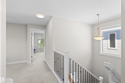 Carpeted landing with white baseboards, a white banister with black iron spindles, and a window with white trim - 4673 Alwood Way, Edmonton, AB 