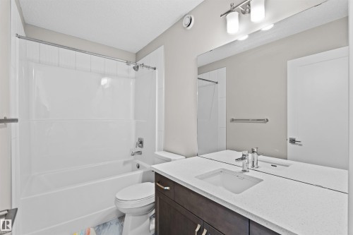 Bathroom featuring a white bathtub/shower combination, white vanity countertop, integrated sink, chrome fixtures, and a dark wood-finish vanity with drawer pulls - 4673 Alwood Way, Edmonton, AB 
