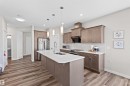 Modern kitchen featuring an expansive center island with an undermount sink, pendant lighting, wood-finish flooring, and shaker-style cabinetry with stainless steel appliances - 4673 Alwood Way, Edmonton, AB 