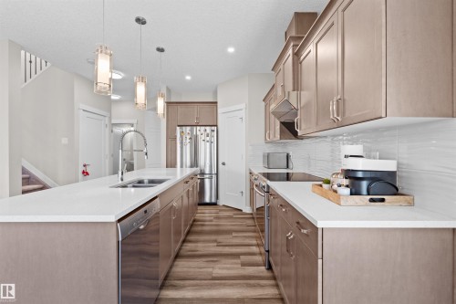 Modern kitchen featuring a spacious island with an undermount sink, stainless steel appliances, wood-finish flooring, light-toned cabinetry, and a textured tile backsplash - 4673 Alwood Way, Edmonton, AB 