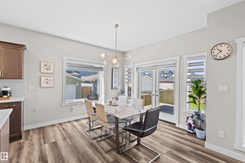 Dining area featuring wood-finish flooring, a contemporary chandelier, multiple windows, and a glass-paneled double door leading to an outdoor space - 4673 Alwood Way, Edmonton, AB 