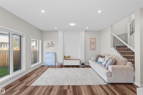 Spacious living area featuring wood-finish flooring, recessed lighting, and large windows - 4673 Alwood Way, Edmonton, AB 