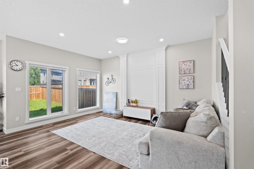 Living area featuring wood-finish flooring, two large windows, recessed lighting, and a white accent wall with panel molding - 4673 Alwood Way, Edmonton, AB 