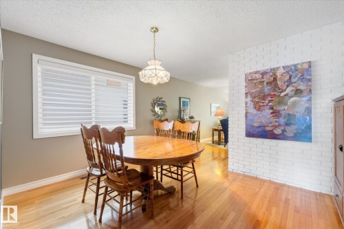 Dining area featuring wood-finish flooring, a white brick accent wall, and a large window with white blinds - 14309 101 Avenue, Edmonton, AB 